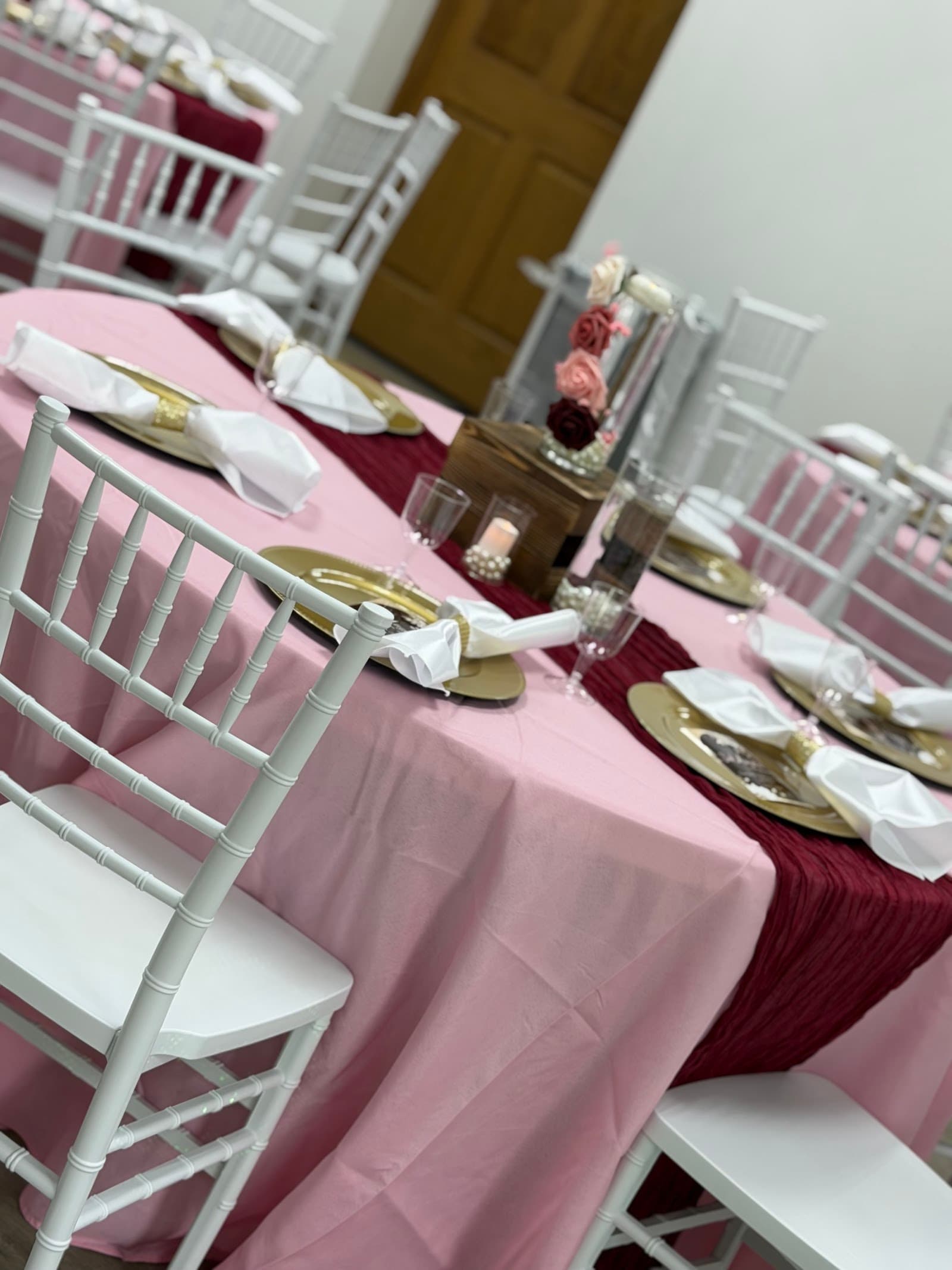 White Chiavari chairs and a set table with gold chargers and a burgundy runner