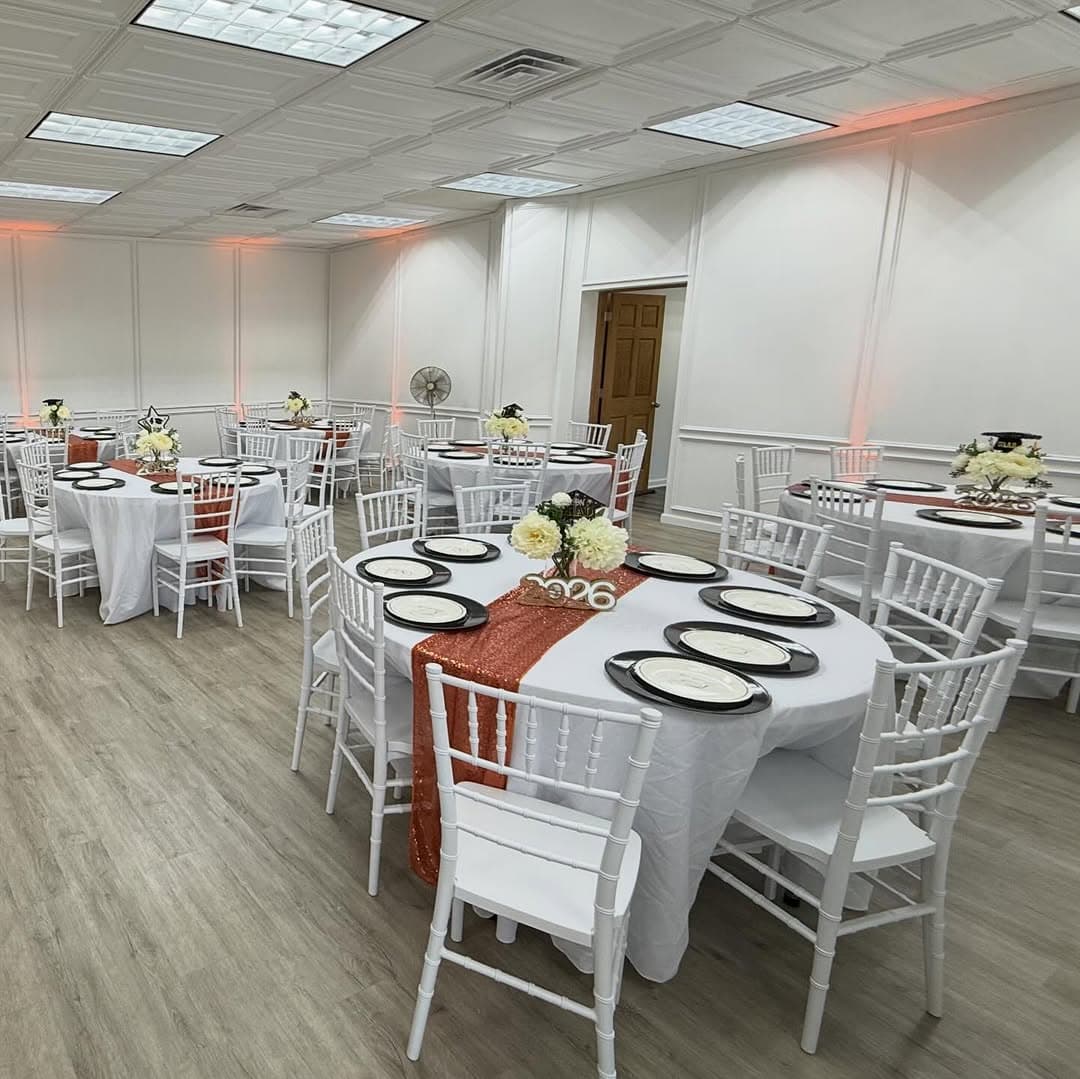 Round tables with white chairs and terracotta runners under warm uplighting in the Ehnita Suite, framed by the room's white panel moulding