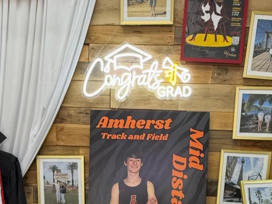 The Congrats Grad neon sign lit above a graduation photo display on the wood accent wall