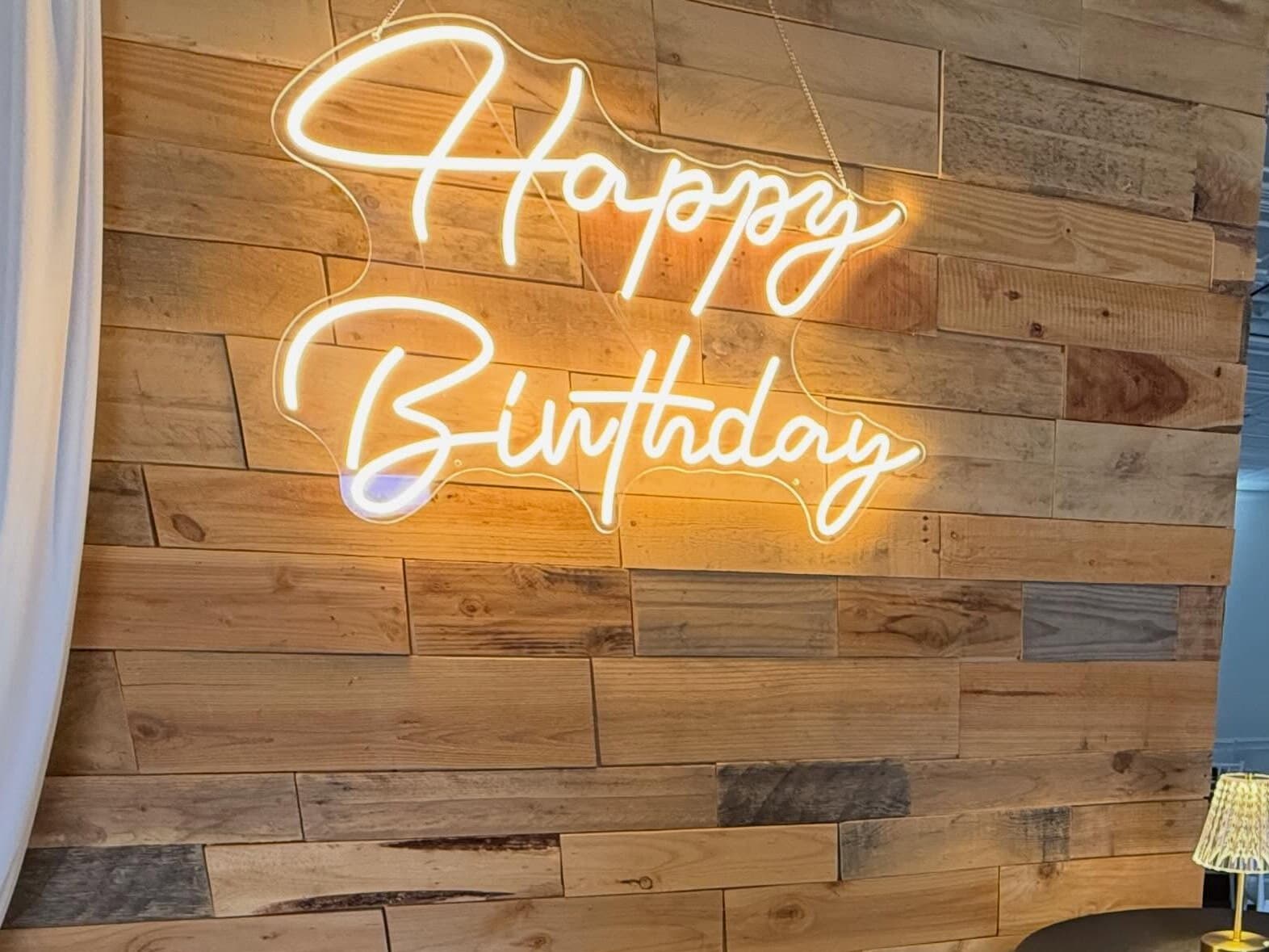 The Happy Birthday neon sign glowing warm over the wood accent wall, with a cocktail table below