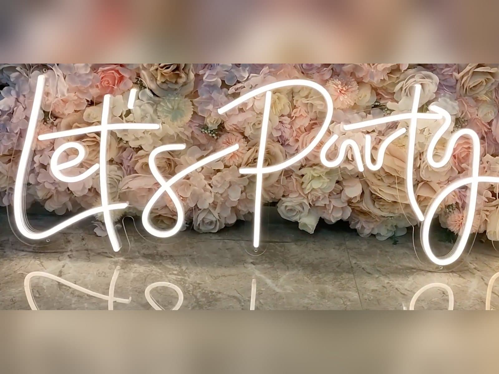 The Let's Party neon sign in white script lit across the flower wall